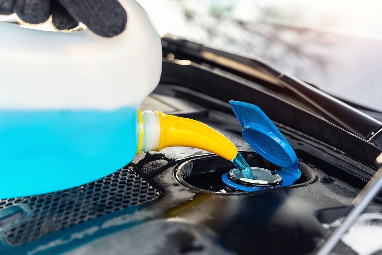 driver-hand-in-gloves-pouring-blue-antifreeze
